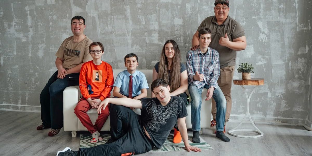 Group of seven people posing casually in a stylish indoor setting with a concrete wall background.