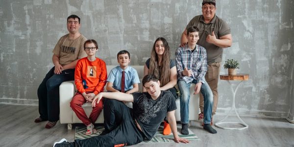 Group of seven people posing casually in a stylish indoor setting with a concrete wall background.