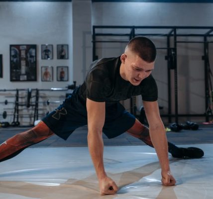 A male athlete stretches intensely in a dimly lit gym environment, preparing for training.